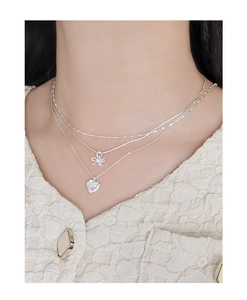 Detail of layered S925 silver necklace with bow pendant and pink zircon heart charm