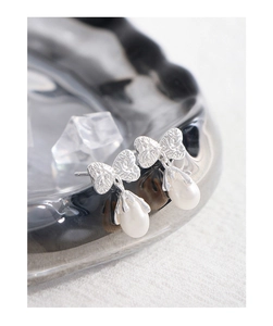 Macro detail of silver butterfly earrings with a hammer-textured finish and pearl drop