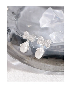 Detail of silver bow earrings with textured surface and drop-shaped white pearl charm