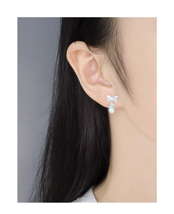 Detailed close-up of a silver bow earring with a natural drop pearl on a model's ear