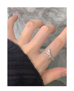 Close-up of a silver irregular liquid metal bow ring on a finger with a lace background
