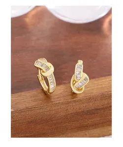 Detail of gold-plated knot stud earrings featuring rectangular-cut zircon stones on wood