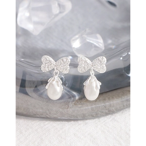 S925 silver bow stud earrings with natural pearls on a luxury glass display