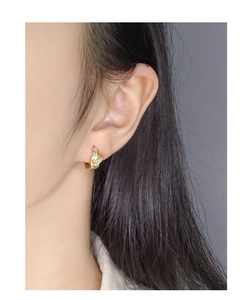Detail view of a gold knot earring with three rectangular zircons worn on the earlobe