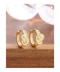 Detail of gold-plated knot hoop earrings with clear baguette zircon stones on wood