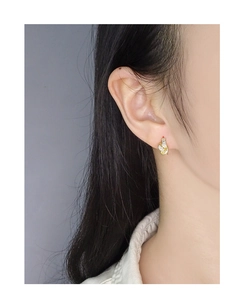 Close-up of golden knotted zircon earring on model ear with minimalist luxury design