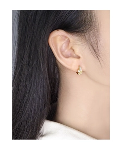 Close-up of gold knotted huggie earring featuring sparkling cubic zirconia on a model's ear