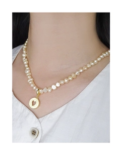 Detailed shot of Baroque pearl necklace featuring a golden heart pendant on a model