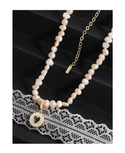 Macro view of Baroque pink pearl necklace with a gold heart pendant on lace