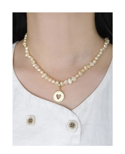 Baroque pearl necklace with gold heart pendant worn on model neck for elegant style