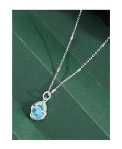 Gros plan d'un pendentif en pierre bleue avec une monture en argent texturé sur fond vert