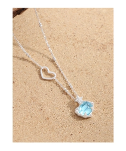 Gros plan sur une chaîne argentée à billes avec cœur et pendentif en cristal bleu clair