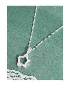 Close-up of a minimalist hollow star pendant in polished silver on a green silk background