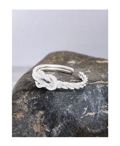 Macro detail of S925 silver nautical knot ring on a dark textured stone background