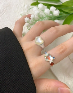 Primo piano di anelli in argento S925 con cuori in conchiglia e cristallo sulla mano