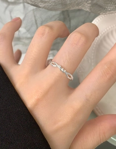Close-up of S925 sterling silver twisted knot ring worn on index finger with fabric background