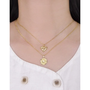 Collier double rang doré avec pendentifs cœur et médaille sur une chemise blanche