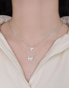 Detail of layered S925 silver necklace with bow and heart pendants on a model neck