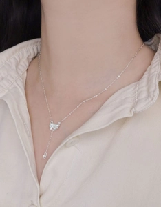 Close-up of S925 silver necklace featuring a bow and heart pendant on model neckline