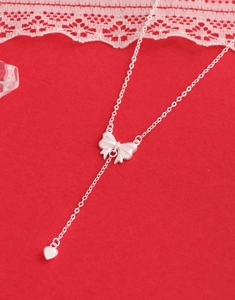 Detail showing S925 silver Y-shaped necklace with bowknot and heart drop on red fabric
