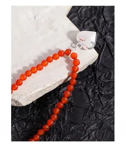 Gros plan des perles en agate rouge et pendentif cœur argenté poli sur fond texturé