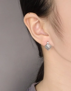 Macro view of a silver shell earring featuring a white pearl on a female model