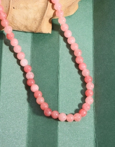 Detailed view of pink agate beads on a green background with a natural dry leaf