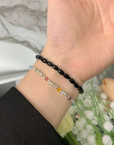 Wrist detail of S925 silver beaded bracelet set with black agate and colored charms