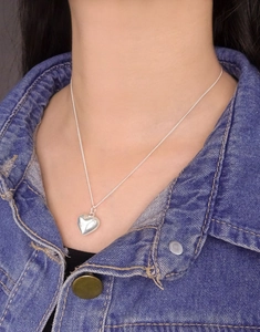 Detail of a polished 3D heart pendant necklace worn with a denim jacket