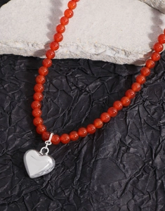 Détail du collier de perles en agate rouge avec un pendentif en forme de cœur argenté