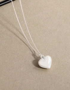 Macro shot of 3D puffy heart pendant in polished silver finish on textured paper