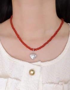 Détail du collier de perles d'agate rouge avec pendentif coeur argenté