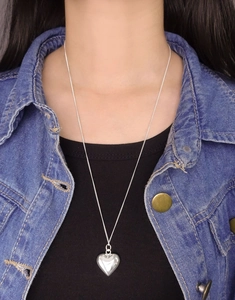 Detail of silver heart pendant necklace worn with a casual denim jacket on model