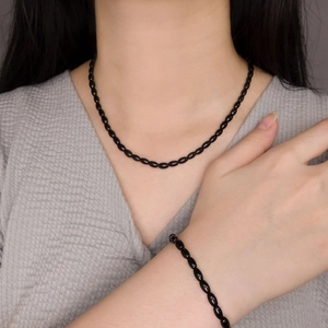 Modern black onyx beaded necklace and bracelet set worn by a model on a minimalist background