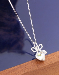 Macro shot of silver bow pendant with heart-shaped moonstone on minimalist cross chain