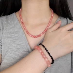 Pink agate beaded necklace and sterling silver bracelets worn by model on grey background