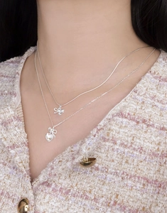Close-up of layered S925 silver necklaces with bow and heart moonstone pendants on a model