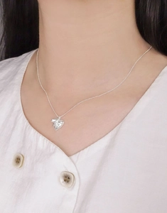 Gros plan du pendentif cœur en argent avec design plissé sur une fine chaîne maille