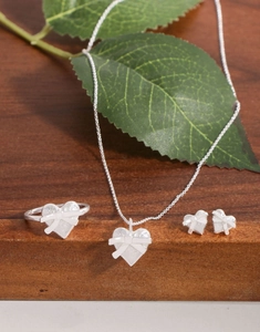 Parure de bijoux coeur en argent avec détails nœud sur une surface en bois naturel