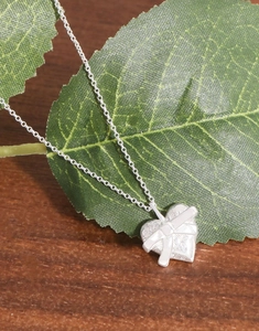 Détail macro du collier cœur en argent S925 avec nœud sur feuille naturelle et bois