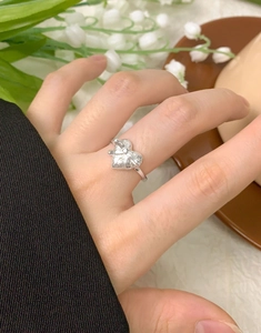 Macro view of a S925 silver bow heart ring worn on a finger with lily of the valley