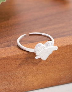 Macro shot of silver heart ring with bow detail on a natural wood surface texture