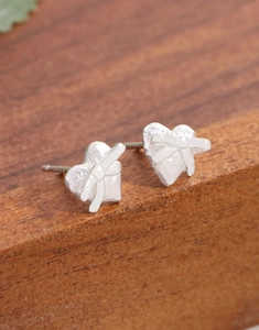 Détail de boucles d'oreilles cœur en argent S925 avec nœud sur fond en bois sombre