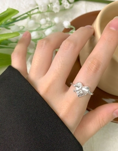 Close-up of S925 silver heart ring with bow detail worn against lily background