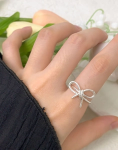 Gros plan d'une bague nœud minimaliste en argent sterling S925 portée au doigt avec fleurs