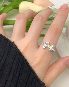 Macro shot of silver bow ring with marquise zircon on finger against tulips