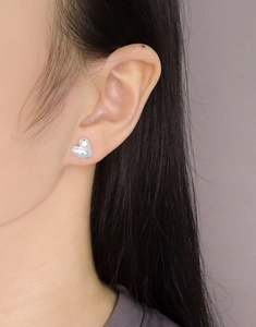 Gros plan de boucles d'oreilles cœur en argent avec texture mate sur l'oreille