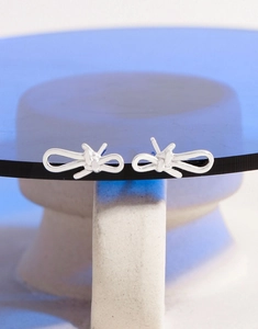 Detail of silver S925 asymmetric bow earrings with a polished ribbon design on blue glass