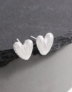 Gros plan de boucles d'oreilles cœur en argent texturé sur une surface en pierre