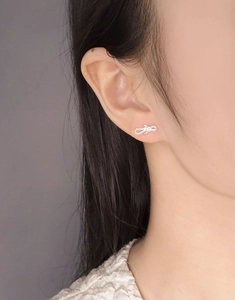 Close-up of minimalist S925 sterling silver bow earrings worn to show delicate wire texture